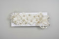Ivory headband with floral patterns, pearl-like beads, and metallic accents displayed on a wicker surface.