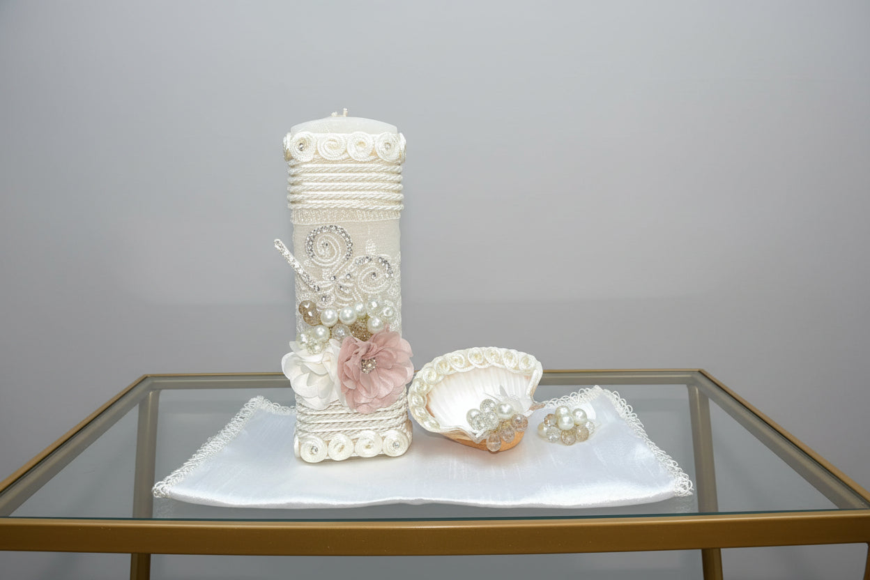 A decorated ivory candle set against a floral background, part of a 3 piece candle set including a shell hankerchief and a pearl necklace.