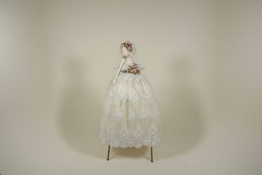 Elegant beige evening gown with floral details on a mannequin against a white draped background