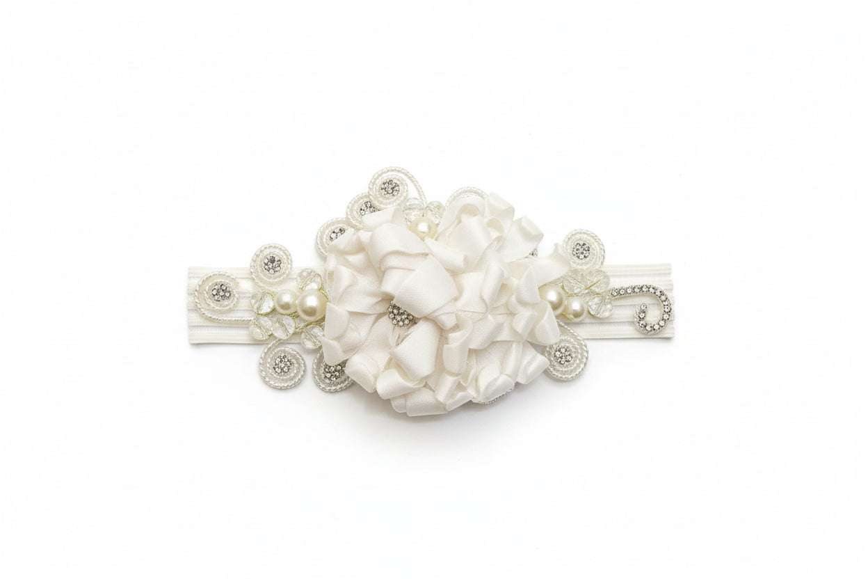 An ivory headband with a floral pattern and embellishments, displayed on a wicker surface.