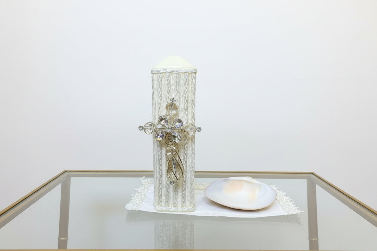 A 3 piece cross baptism candle set in ivory color, displayed against a floral background. The set includes a decorated candle, a natural shell, and a handkerchief.