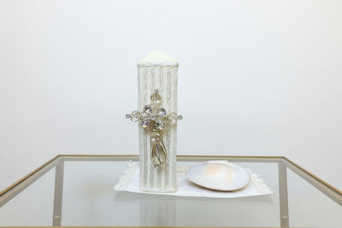 A 3 piece cross baptism candle set in ivory color, displayed against a floral background. The set includes a decorated candle, a natural shell, and a handkerchief.