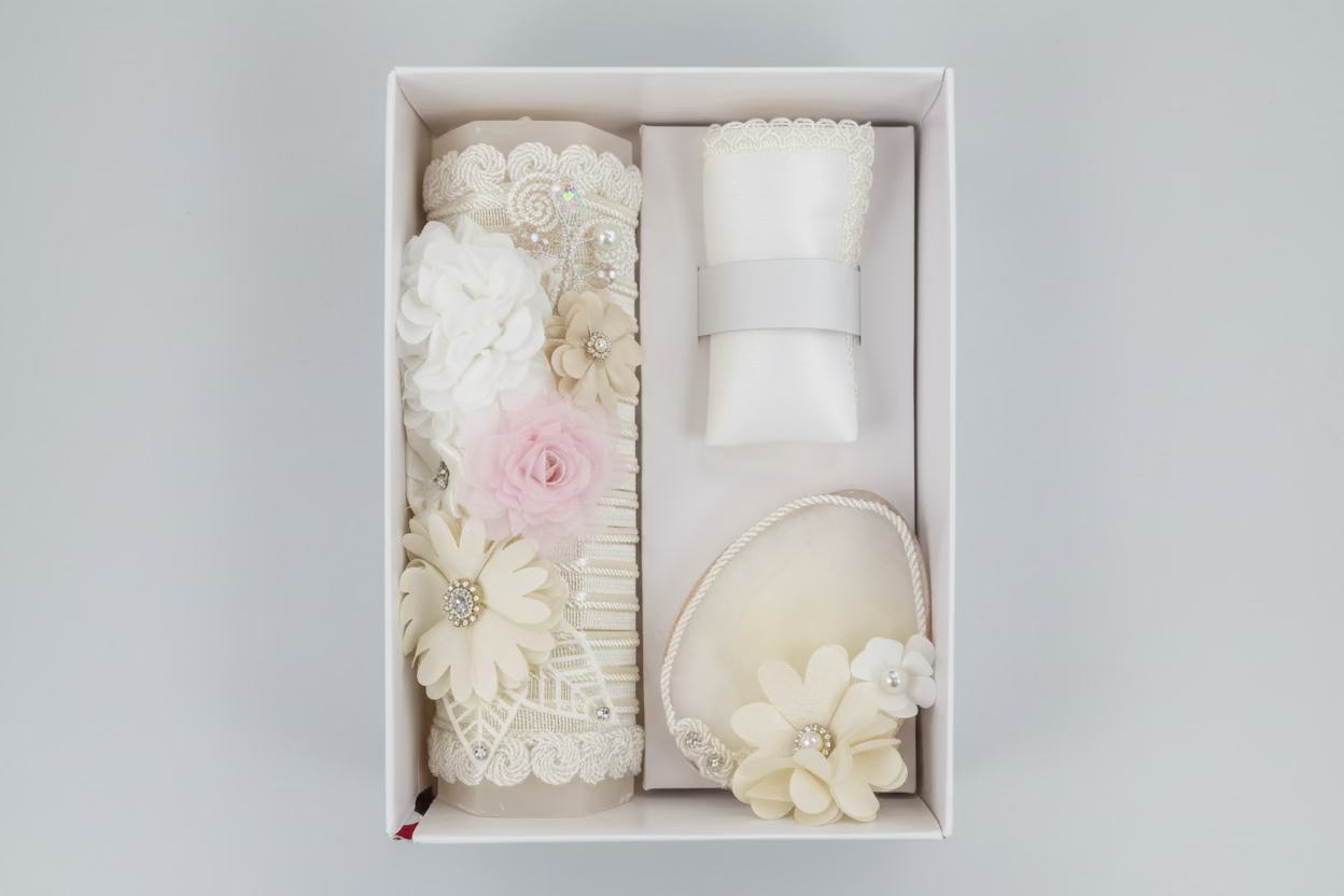 A 3 piece girl baptism candle set in ivory, including a decorated candle with floral patterns, a shell, and a hankerchief, all displayed in an open box.