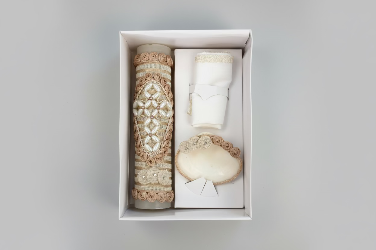 A 3 piece candle set for boys, including a decorated beige candle, a natural shell, and a hankerchief, presented in an open box with a pink interior lining.